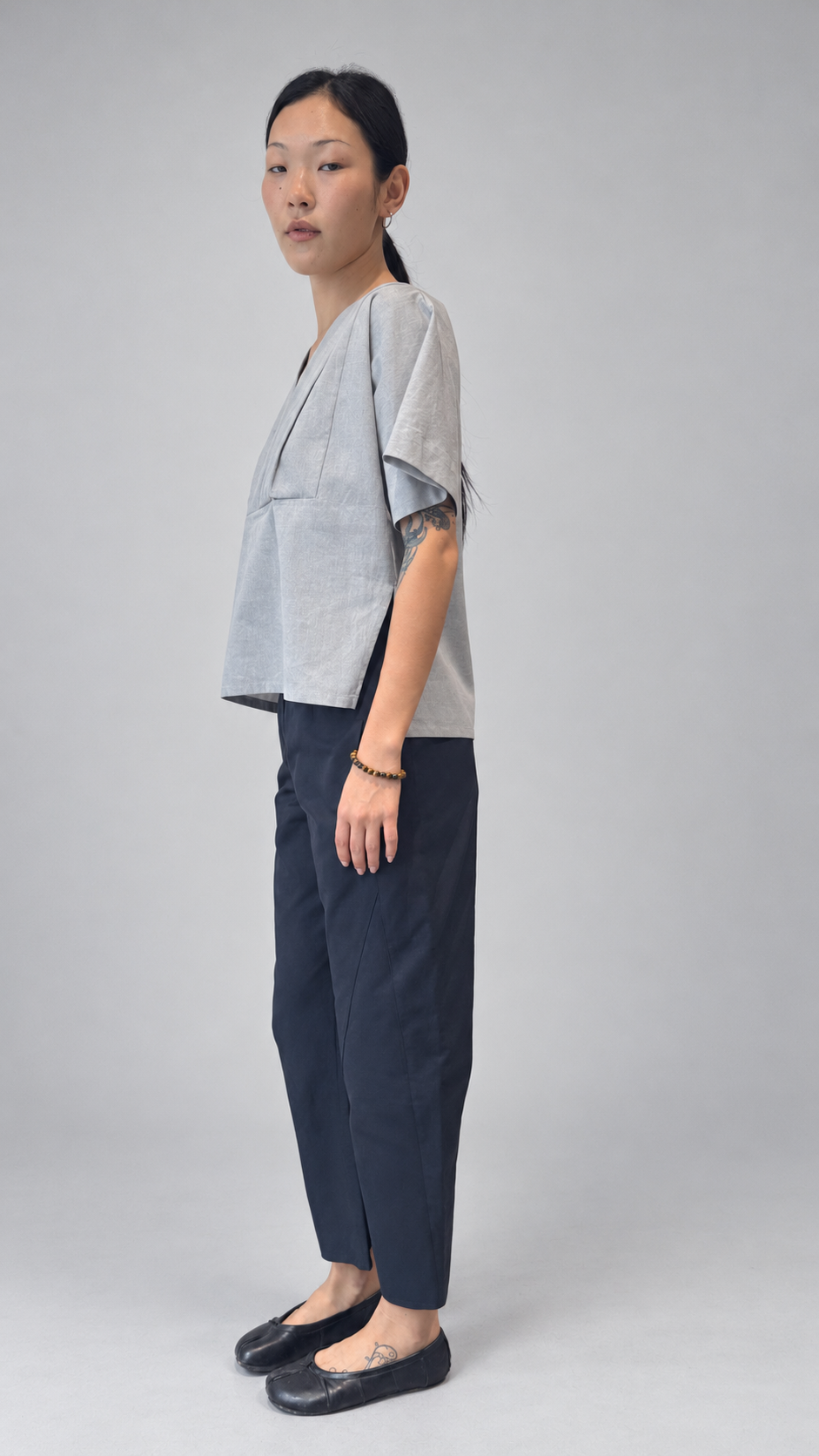 Lotus Shirt, Temple Grey — angled model view. Anujin wearing lotus shirt temple grey, twist pants berge.