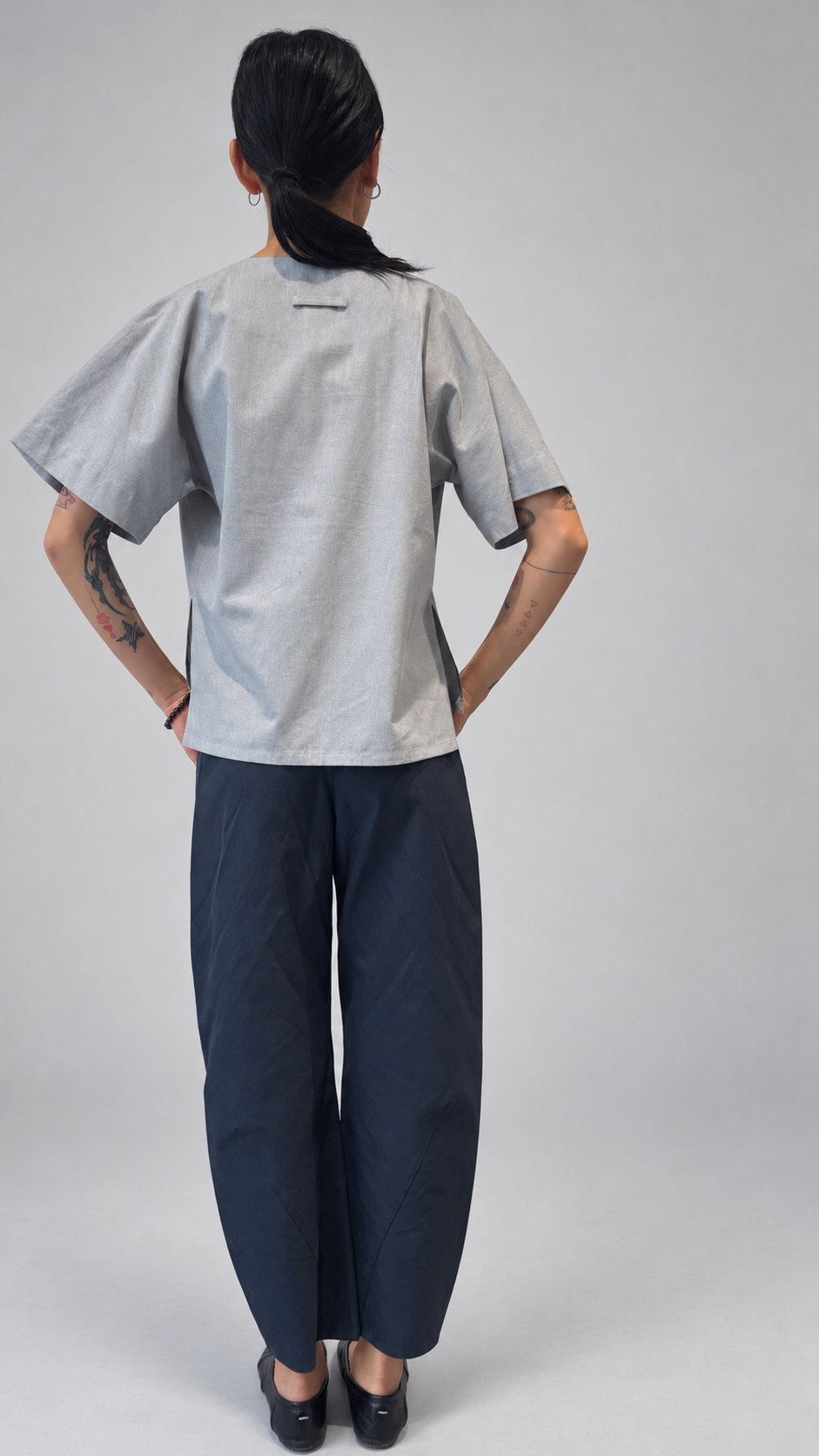 Lotus Shirt, Temple Grey — back model view. Anujin wearing lotus shirt temple grey, twist pants berge.
